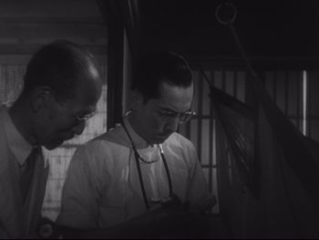 Movie still from “Stray Dog” (1949), directed by Akira Kurosawa – Two men looking at a computer screen in black and white; Medium shot, Low angle