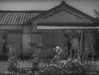 Movie still from “Stray Dog” (1949), directed by Akira Kurosawa – An old black and white photo of two people in front of a house; Extreme Wide shot, High angle
