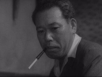 Movie still from “Stray Dog” (1949), directed by Akira Kurosawa – An older man smoking a cigarette in a black and white photo; Close Up shot, Low angle