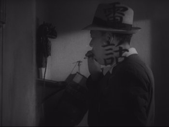 Movie still from “Stray Dog” (1949), directed by Akira Kurosawa – A man in a hat is smoking a cigarette in front of a mirror; Close Up shot, High angle