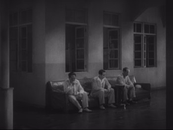 Movie still from “Stray Dog” (1949), directed by Akira Kurosawa – A group of men sitting on top of couches in a room; Wide shot, High angle