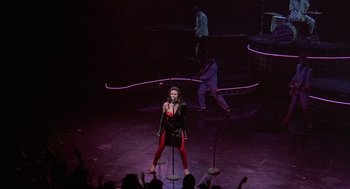 Movie still from “Streets of Fire” (1984), directed by Walter Hill – A woman is singing on a stage with a microphone; Wide shot, High angle