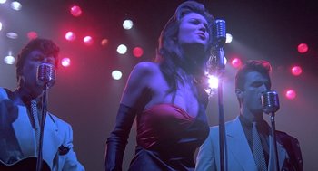 Movie still from “Streets of Fire” (1984), directed by Walter Hill – A woman in a red dress singing into a microphone; Medium shot, Low angle