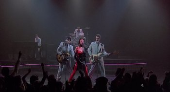 Movie still from “Streets of Fire” (1984), directed by Walter Hill – A group of people on a stage with a woman in red; Wide shot, Low angle