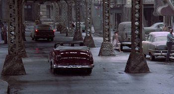 Movie still from “Streets of Fire” (1984), directed by Walter Hill – A red car driving down a street next to trees; Extreme Wide shot, High angle