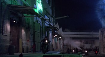 Movie still from “Streets of Fire” (1984), directed by Walter Hill – A man riding a motorcycle down a street at night; Extreme Wide shot, Low angle