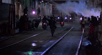 Movie still from “Streets of Fire” (1984), directed by Walter Hill – A group of people riding motorcycles down a train track at night; Extreme Wide shot, High angle