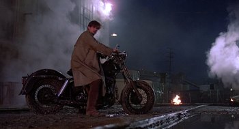 Movie still from “Streets of Fire” (1984), directed by Walter Hill – A man standing next to a motorcycle on the side of the road; Wide shot, Low angle