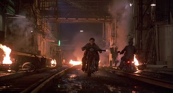 Movie still from “Streets of Fire” (1984), directed by Walter Hill – A man riding a motorcycle down the middle of a street; Wide shot, Low angle