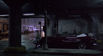 Movie still from “Streets of Fire” (1984), directed by Walter Hill – Two people standing next to a car in a parking lot; Wide shot, High angle