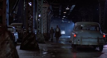 Movie still from “Streets of Fire” (1984), directed by Walter Hill – Two people walking down a dark street with a car in front of them; Wide shot, Low angle