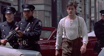 Movie still from “Streets of Fire” (1984), directed by Walter Hill – A man in suspenders standing next to a police officer; Medium shot, Low angle