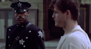 Movie still from “Streets of Fire” (1984), directed by Walter Hill – A police officer standing next to a man in a white shirt; Medium shot, Over the shoulder angle