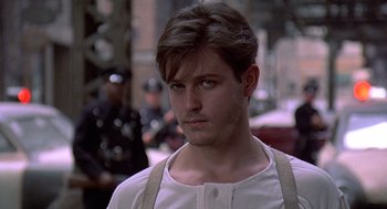 Movie still from “Streets of Fire” (1984), directed by Walter Hill – A young man in a white shirt is standing in the street; Close Up shot, Over the shoulder angle