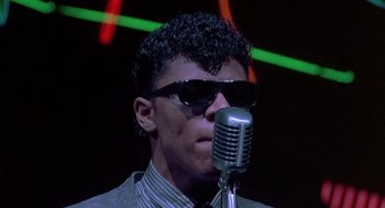Movie still from “Streets of Fire” (1984), directed by Walter Hill – A man with sunglasses and a microphone in front of him; Close Up shot, Low angle