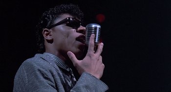Movie still from “Streets of Fire” (1984), directed by Walter Hill – A man in a gray jacket holding up a microphone; Close Up shot, Low angle