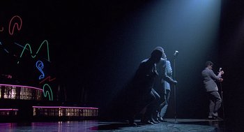 Movie still from “Streets of Fire” (1984), directed by Walter Hill – A couple of people that are on a stage with a microphone; Wide shot, Low angle