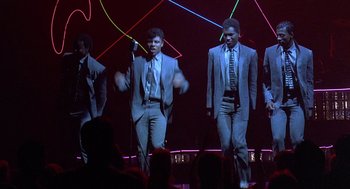 Movie still from “Streets of Fire” (1984), directed by Walter Hill – A group of men in suits and ties on a stage; Wide shot, Low angle