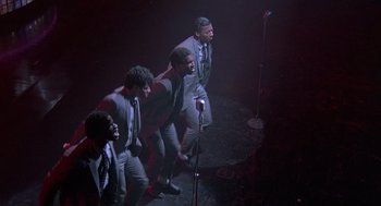 Movie still from “Streets of Fire” (1984), directed by Walter Hill – A group of men standing next to each other on a stage with microphones; Wide shot, High angle