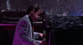 Movie still from “Streets of Fire” (1984), directed by Walter Hill – A man in a white jacket playing a piano; Medium shot, High angle