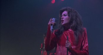 Movie still from “Streets of Fire” (1984), directed by Walter Hill – A woman in a red dress singing into a microphone on a stage; Medium shot, Low angle