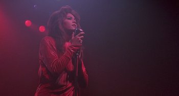 Movie still from “Streets of Fire” (1984), directed by Walter Hill – A woman in a red dress holding a microphone in her hand; Medium shot, Low angle