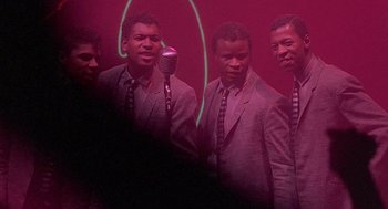 Movie still from “Streets of Fire” (1984), directed by Walter Hill – A group of men standing next to each other in front of a microphone; Medium shot, High angle