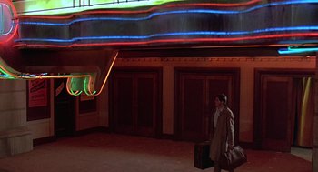 Movie still from “Streets of Fire” (1984), directed by Walter Hill – A man in a suit carrying a suitcase in front of a neon sign; Wide shot, Low angle