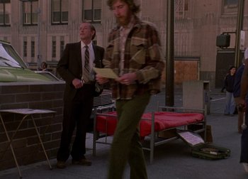 A man in a plaid shirt and a suit is walking outside