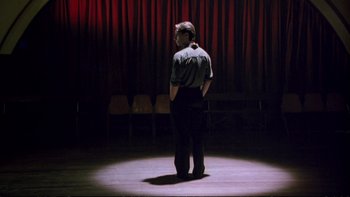 Movie still from “Strictly Ballroom” (1992), directed by Baz Luhrmann – A man standing in a circle in front of a red curtain; Wide shot, Low angle