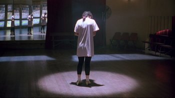 Movie still from “Strictly Ballroom” (1992), directed by Baz Luhrmann – A person standing in a room with their hands behind their head; Wide shot, Low angle