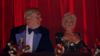 Movie still from “Strictly Ballroom” (1992), directed by Baz Luhrmann – A man and a woman sitting in front of a red curtain; Medium shot, Low angle