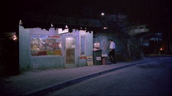 Movie still from “Strictly Ballroom” (1992), directed by Baz Luhrmann – A man standing on the side of the street near a store; Wide shot, High angle