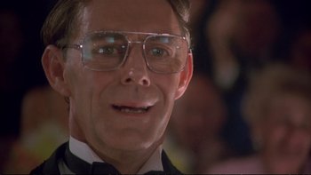 Movie still from “Strictly Ballroom” (1992), directed by Baz Luhrmann – A person wearing glasses and a suit; Close Up shot, Low angle