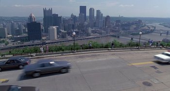 Movie still from “Striking Distance” (1993), directed by Rowdy Herrington – A car driving down a street with a view of a city; Extreme Wide shot, High angle