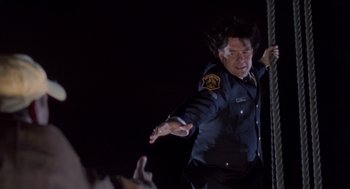 Movie still from “Striking Distance” (1993), directed by Rowdy Herrington – A man in a police officer's uniform throws his hands in the air; Medium shot, Low angle