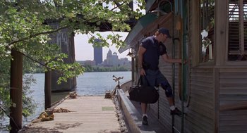 Movie still from “Striking Distance” (1993), directed by Rowdy Herrington – A man holding a bag while standing on a dock; Wide shot, High angle