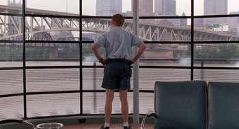 Movie still from “Striking Distance” (1993), directed by Rowdy Herrington – A man standing in front of a window looking out at a city; Wide shot, Low angle