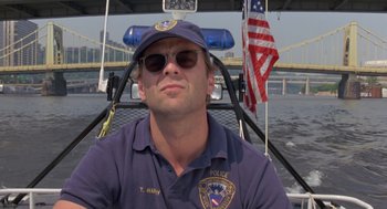 Movie still from “Striking Distance” (1993), directed by Rowdy Herrington – A police officer is sitting on a boat in the water; Close Up shot, Low angle