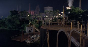 Movie still from “Striking Distance” (1993), directed by Rowdy Herrington – A view of a factory at night with a boat in the foreground; Extreme Wide shot, High angle