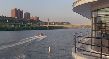 Movie still from “Striking Distance” (1993), directed by Rowdy Herrington – A boat traveling down a river next to a bridge; Extreme Wide shot, High angle