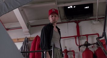 Movie still from “Striking Distance” (1993), directed by Rowdy Herrington – A man wearing a red hat standing next to a fire hydrant; Medium shot, Low angle