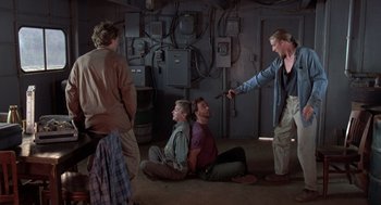 Movie still from “Striking Distance” (1993), directed by Rowdy Herrington – A group of people sitting on the ground in a room; Wide shot, Over the shoulder angle