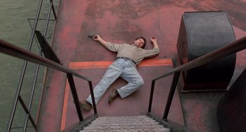 Movie still from “Striking Distance” (1993), directed by Rowdy Herrington – A man laying on the ground holding a cell phone; Wide shot, Overhead angle