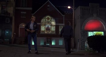 Movie still from “Striking Distance” (1993), directed by Rowdy Herrington – Two people walking on the sidewalk at night; Wide shot, Low angle