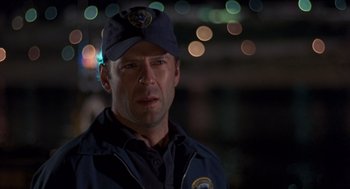 Movie still from “Striking Distance” (1993), directed by Rowdy Herrington – A man in a police uniform is standing in the dark; Close Up shot, Over the shoulder angle