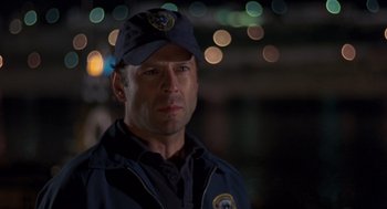 Movie still from “Striking Distance” (1993), directed by Rowdy Herrington – A man wearing a police uniform with lights in the background; Close Up shot, Over the shoulder angle