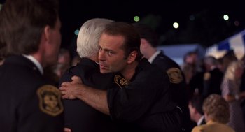 Movie still from “Striking Distance” (1993), directed by Rowdy Herrington – A man hugging another man in front of a group of people; Close Up shot, Over the shoulder angle