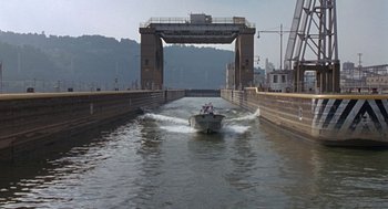 Movie still from “Striking Distance” (1993), directed by Rowdy Herrington – A boat traveling down a river near a bridge; Extreme Wide shot, High angle