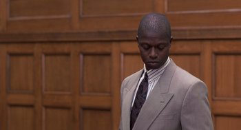 Movie still from “Striking Distance” (1993), directed by Rowdy Herrington – A man wearing a suit and tie standing in front of a wall; Medium shot, Low angle